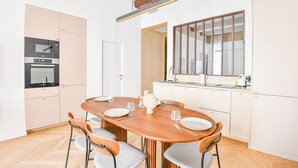 Une cuisine moderne avec des meubles blancs, une table à manger en bois et une grande fenêtre.