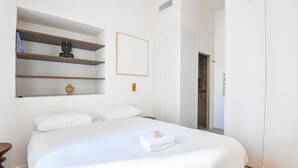 Une chambre à coucher avec un grand lit, une étagère en bois, un tableau encadré et une porte donnant sur une salle de bain.
