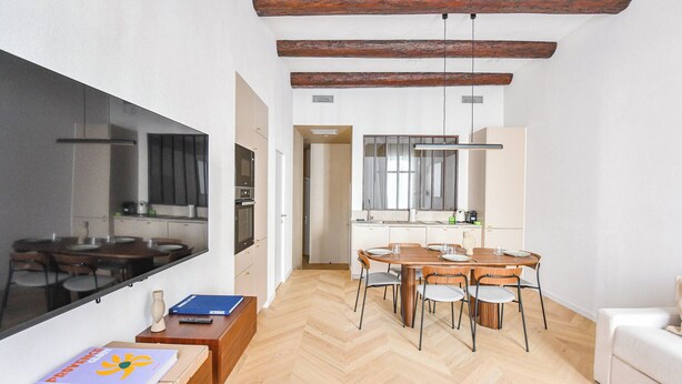 Une cuisine moderne dotée d’une grande fenêtre, de poutres en bois et d’un coin repas avec un parquet disposé en motif à chevrons.