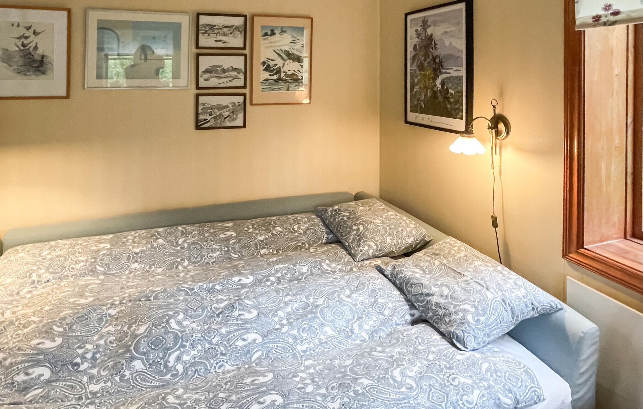 Una cama con ropa de cama estampada, una lámpara fijada a la pared y varias fotografías enmarcadas.