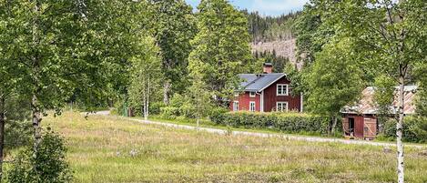 Et rødt hus omgivet af frodigt grønt og træer.