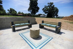 Two benches with cushions, a stone planter, and a patterned rug on a concrete surface. - Minutes to I-65! Clean Modern Home: Trail ride, Stargaze, Firepit &more (Elizabethtown)