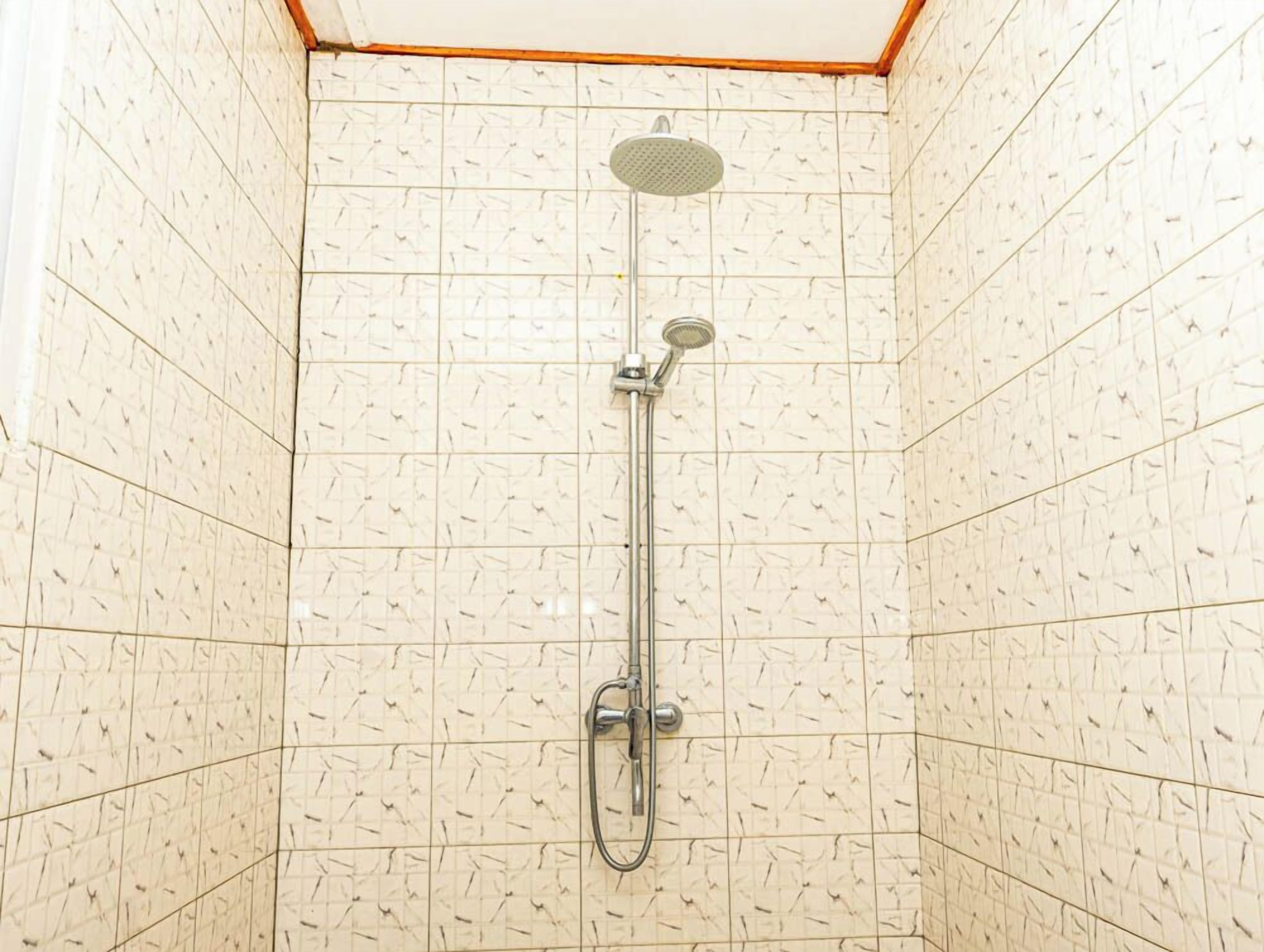 A shower with a handheld showerhead and a wall-mounted faucet in a tiled room.