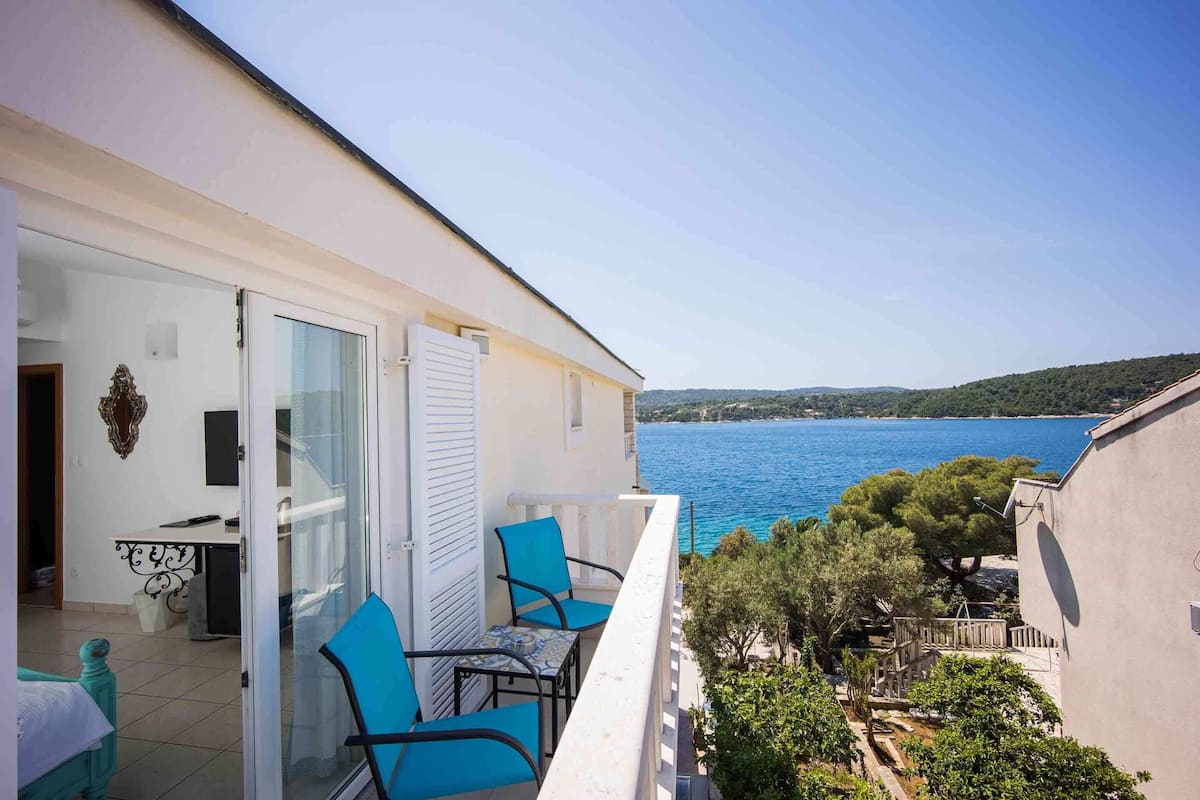 A balcony with a table and chairs, overlooking a body of water and greenery.