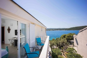 A balcony with a table and chairs, overlooking a body of water and greenery. - Boutique Guesthouse Sveti Petar (Solta)