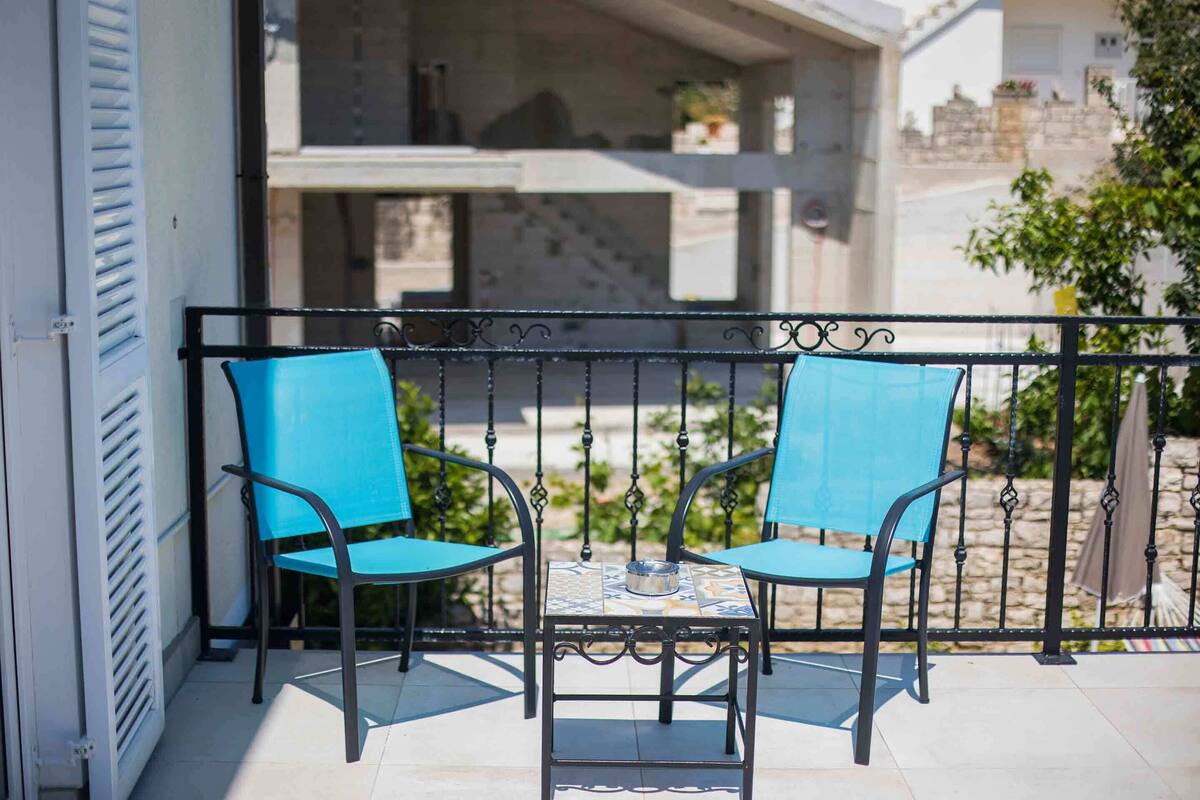 A balcony with two blue chairs and a small table with a bowl.