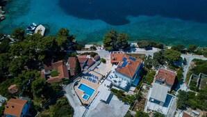 An aerial view of a coastal residential area with houses, a swimming pool, and clear blue waters. - Boutique Guesthouse Sveti Petar (Solta)