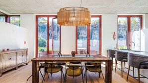 Een eetgedeelte met een houten tafel, vier stoelen, een hanglamp en grote ramen met uitzicht op groen.