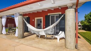A covered patio with a hammock, outdoor furniture, and a red building with shutters. - Stunning home in Marza (Marza)