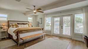 Une chambre à coucher comprenant un lit, un ventilateur de plafond, un banc, une table de chevet et une grande fenêtre avec des stores.