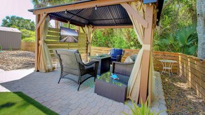 Une terrasse extérieure avec des meubles en osier, une pergola et une vue sur un pont.