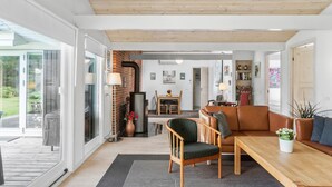Een moderne woonkamer met een houten plafond, een glazen deur naar een buitenruimte, een eettafel met stoelen, en een bank.