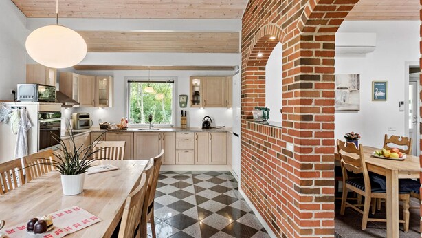 Een moderne keuken met houten kastjes, een bakstenen muur en een eethoek met een geruit vloertje.