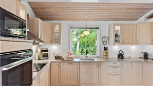 Een moderne keuken met houten kastjes, een inbouwoven, een spoelbak en een raam met uitzicht op groen.
