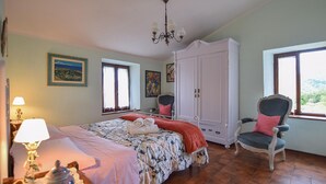 Ein Schlafzimmer mit Bett, Stuhl, Kleiderschrank, einer Deckenleuchte und Bildern an den Wänden.