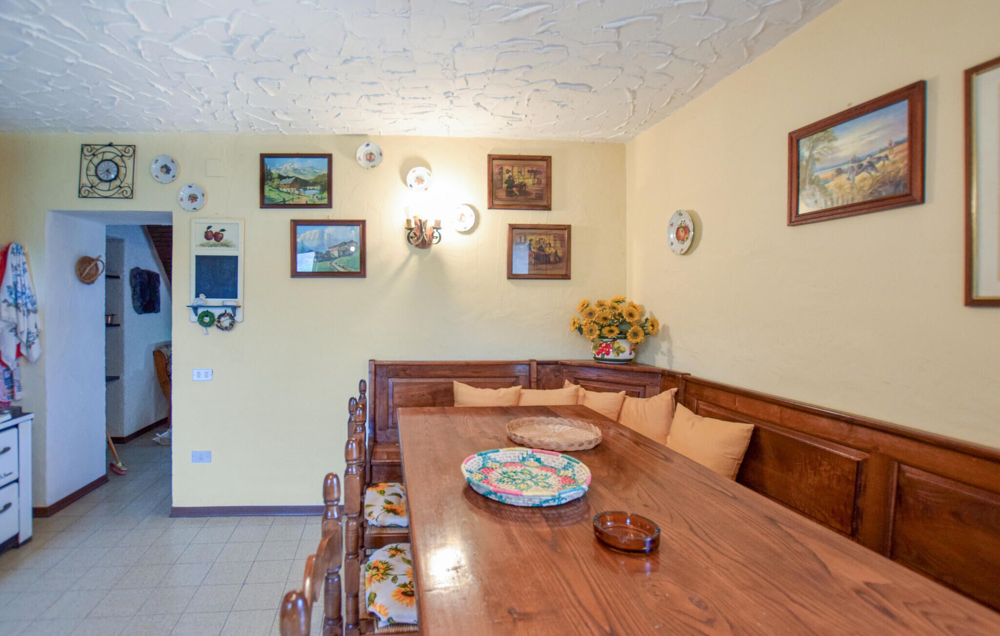 A dining area with a wooden table and benches, surrounded by walls decorated with framed pictures and wall-mounted clocks.