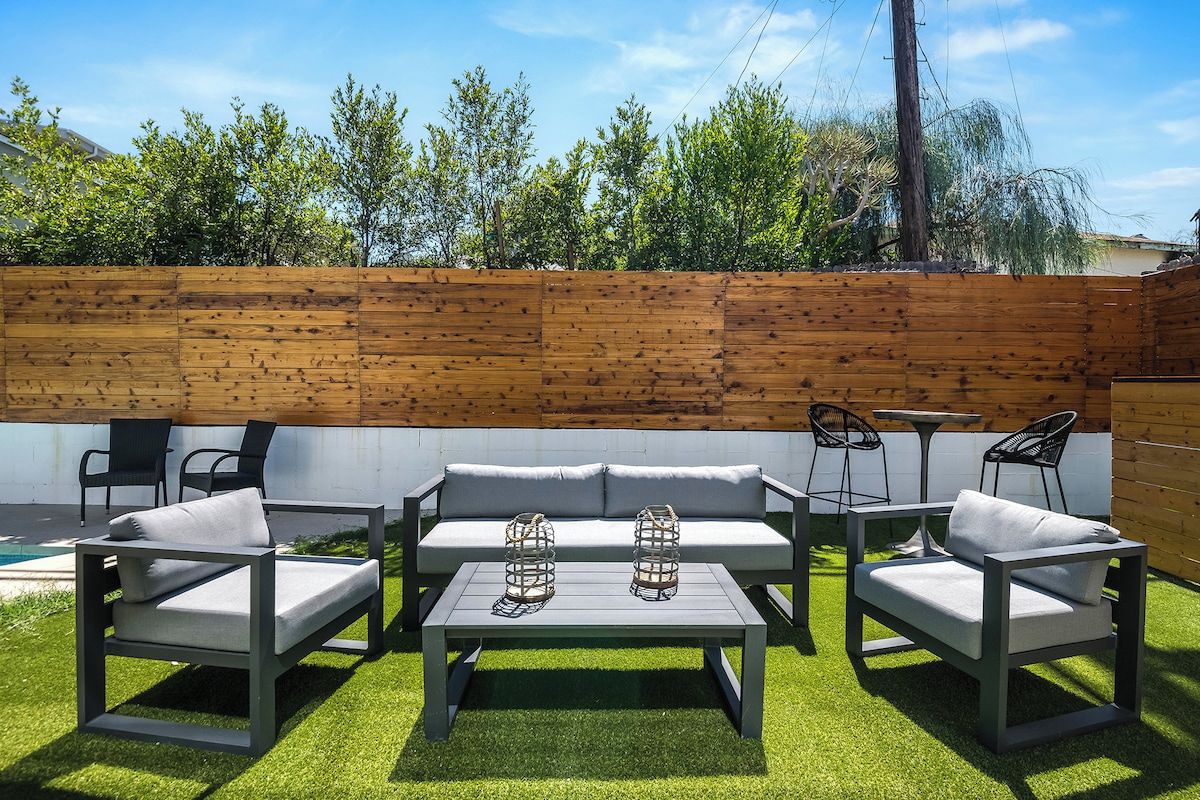 An outdoor patio with a wooden fence, a grey sofa set, a table, and two chairs.