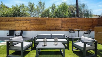 An outdoor patio with a wooden fence, a grey sofa set, a table, and two chairs.