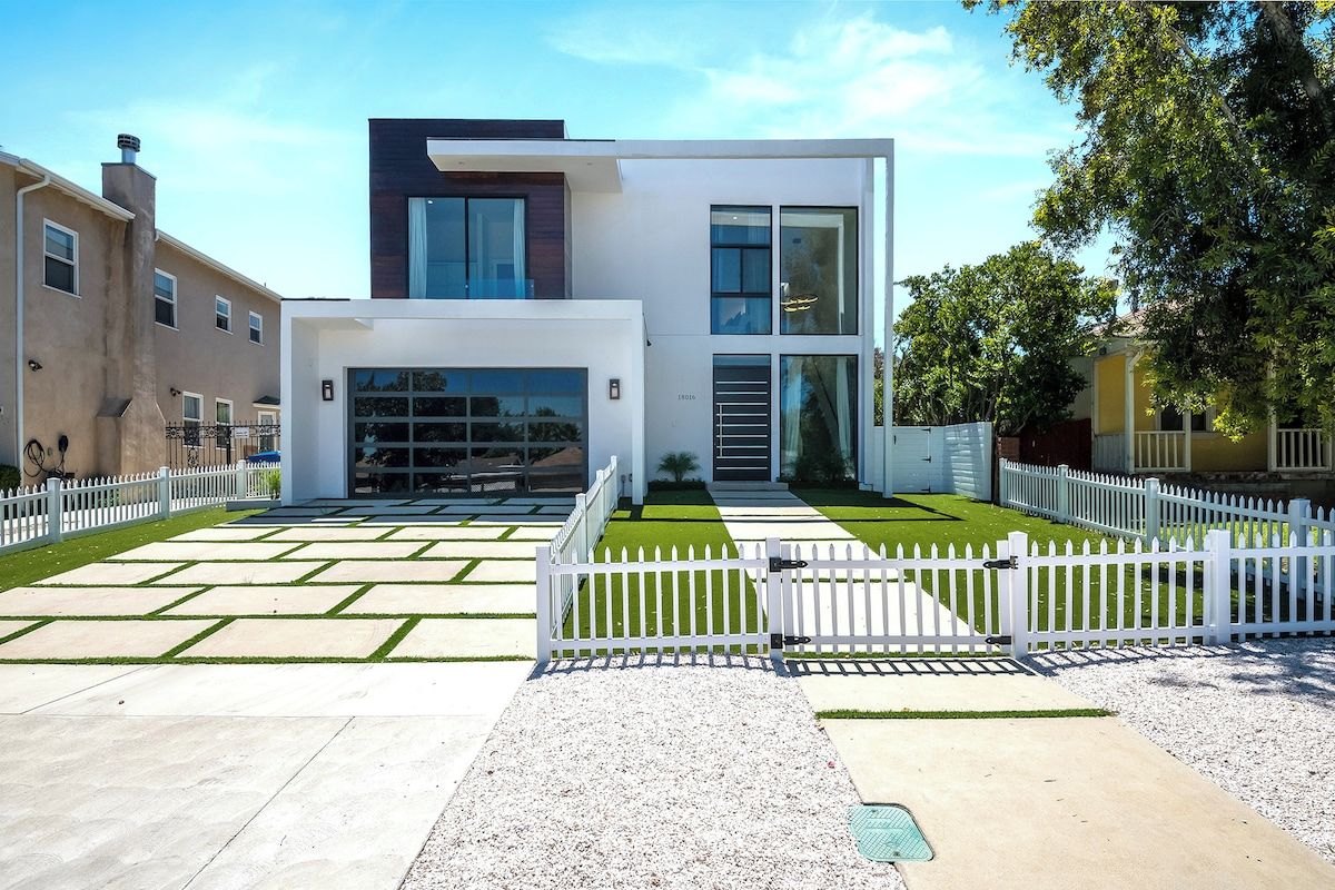 A modern two-story house with a garage, a white picket fence, and a well-maintained lawn.