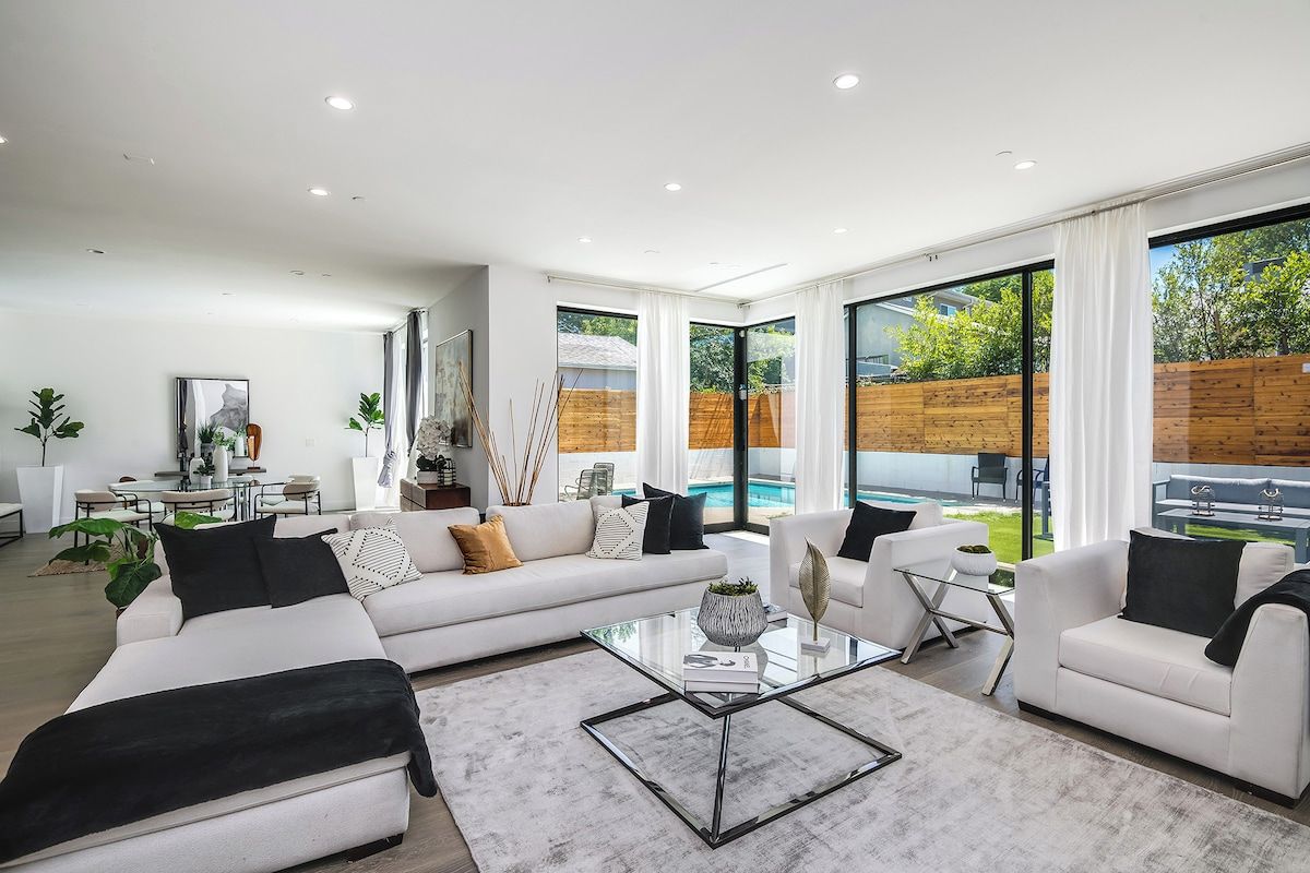 A modern living room with a white sofa, a glass coffee table, and a view of a swimming pool.