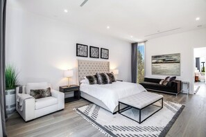 Een moderne slaapkamer met een groot bed, een nachtkastje, een stoel en een schilderij aan de muur.