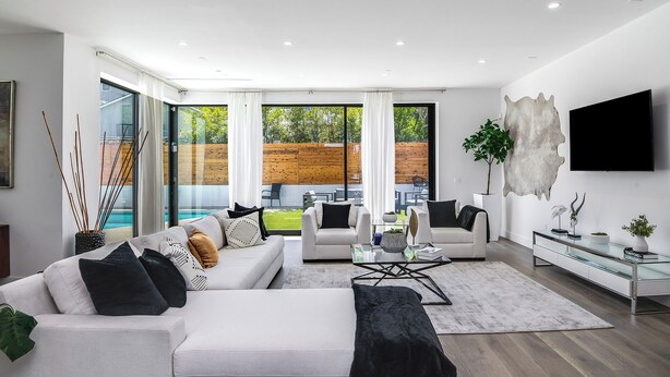 Un salon moderne comprenant un canapé, des fauteuils, une table basse et un téléviseur. Une porte vitrée donne accès à un espace extérieur avec une piscine.
