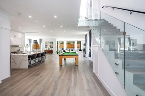 Un interior moderno con mesa de billar, zona de cocina y escalera de cristal.