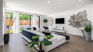 Un salon moderne avec un grand canapé, une table basse en verre et un téléviseur fixé au mur. On y trouve également une grande œuvre d’art abstraite et une plante en pot.