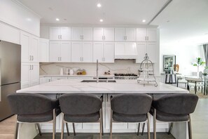 Une cuisine moderne avec des meubles blancs, un îlot central doté de tabourets, un réfrigérateur en acier inoxydable et une cuisinière à gaz.