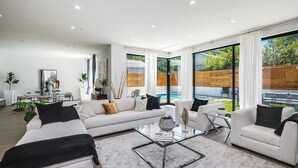 Un salon moderne avec une table basse en verre, des canapés blancs et une vue sur un jardin avec une piscine.