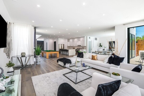 Un salon moderne avec une table basse en verre, un canapé et un coin repas comprenant une table de billard.