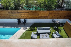 Un espace piscine aménagé sur le toit, avec un mur en bois, deux chaises longues, une petite table et une chaise.