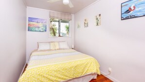 Un dormitorio con cama, ventilador de techo, ventana y decoración en la pared.