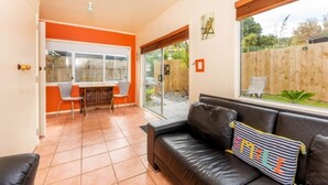 Una sala de estar moderna con un sofá de cuero negro, una mesa de comedor con sillas y un ventanal con vistas al jardín trasero.