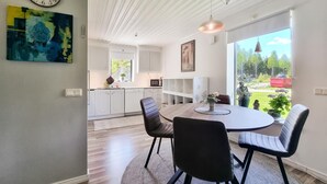 A modern kitchen with white cabinets, a dining area with a round table and chairs, and a large window offering a view of the outdoors.