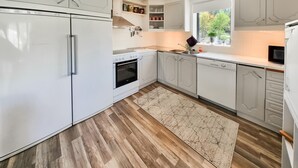 A modern kitchen with white cabinetry, a built-in oven, a dishwasher, and a window providing natural light.