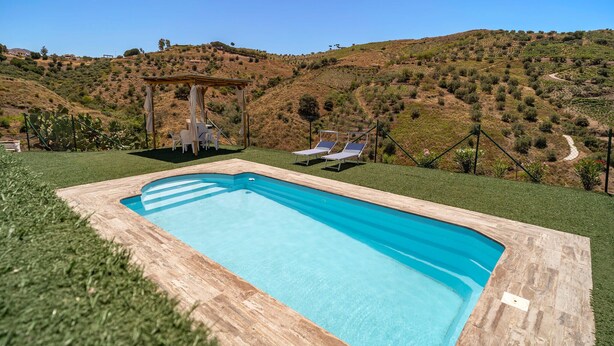 A rectangular swimming pool with a wooden deck, two lounge chairs, a pergola with a table and chairs, and a view of a hilly landscape. - Lovely home in Canillas de Albaidas (Canillas de Albaidas)