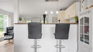 Una cucina moderna con mobili bianchi, un'isola centrale con sgabelli da bar, illuminazione a sospensione e vista sull'esterno.