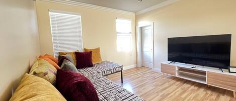 A living room with a sofa set, a flat-screen TV, and a wooden floor.