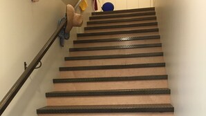 Eine Treppe mit abwechselnden Holzdielen und schwarzen Tritten, einem Geländer und einer Wandleuchte.