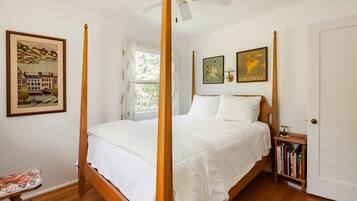 A bedroom with a four-poster bed, a ceiling fan, and a bookshelf with books.