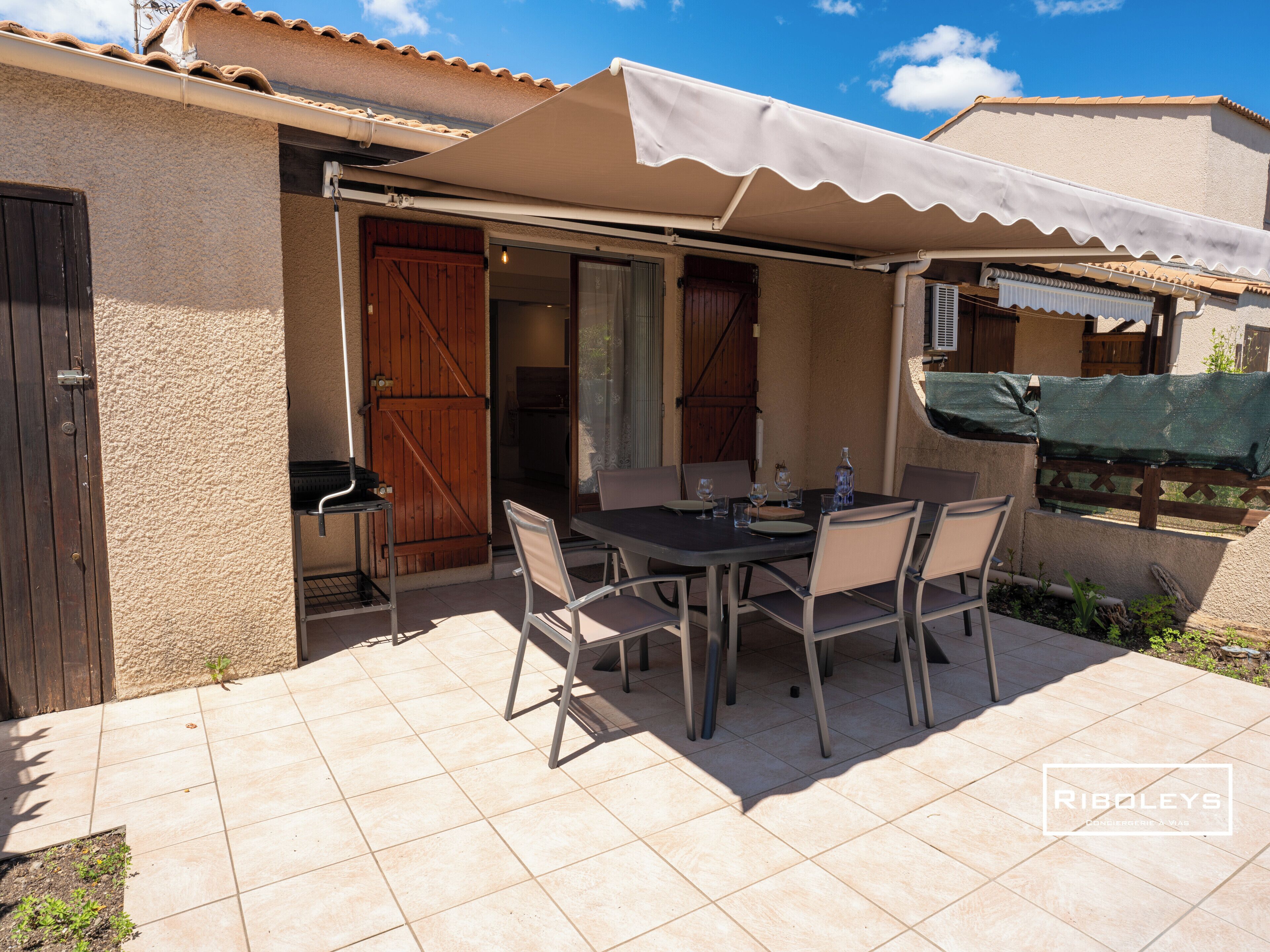 An outdoor patio with a table and chairs, a covered area, and a wooden door.