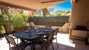 Un patio al aire libre con una mesa dispuesta para comer, rodeada de sillas y una zona de barbacoa.