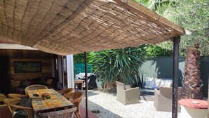 An outdoor patio with wicker furniture, a table with a colorful tablecloth, and a thatched roof. - Cabano for rent by the sea  (Hyères)