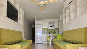 A compact living space with two green sofas, a small kitchenette, and a ceiling fan. - A009 Seaside view Las Vistas TRG Tenerife Royal Gardens (Playa de las Américas)
