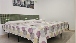 A neatly made bed with a patterned bedspread, a green tiled headboard, and a cityscape painting above it. - A009 Seaside view Las Vistas TRG Tenerife Royal Gardens (Playa de las Américas)
