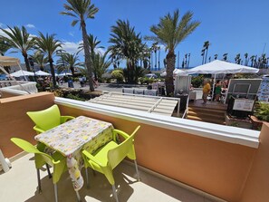 Terraço com mesa e cadeiras, vista para uma rua com palmeiras e áreas de estar ao ar livre.