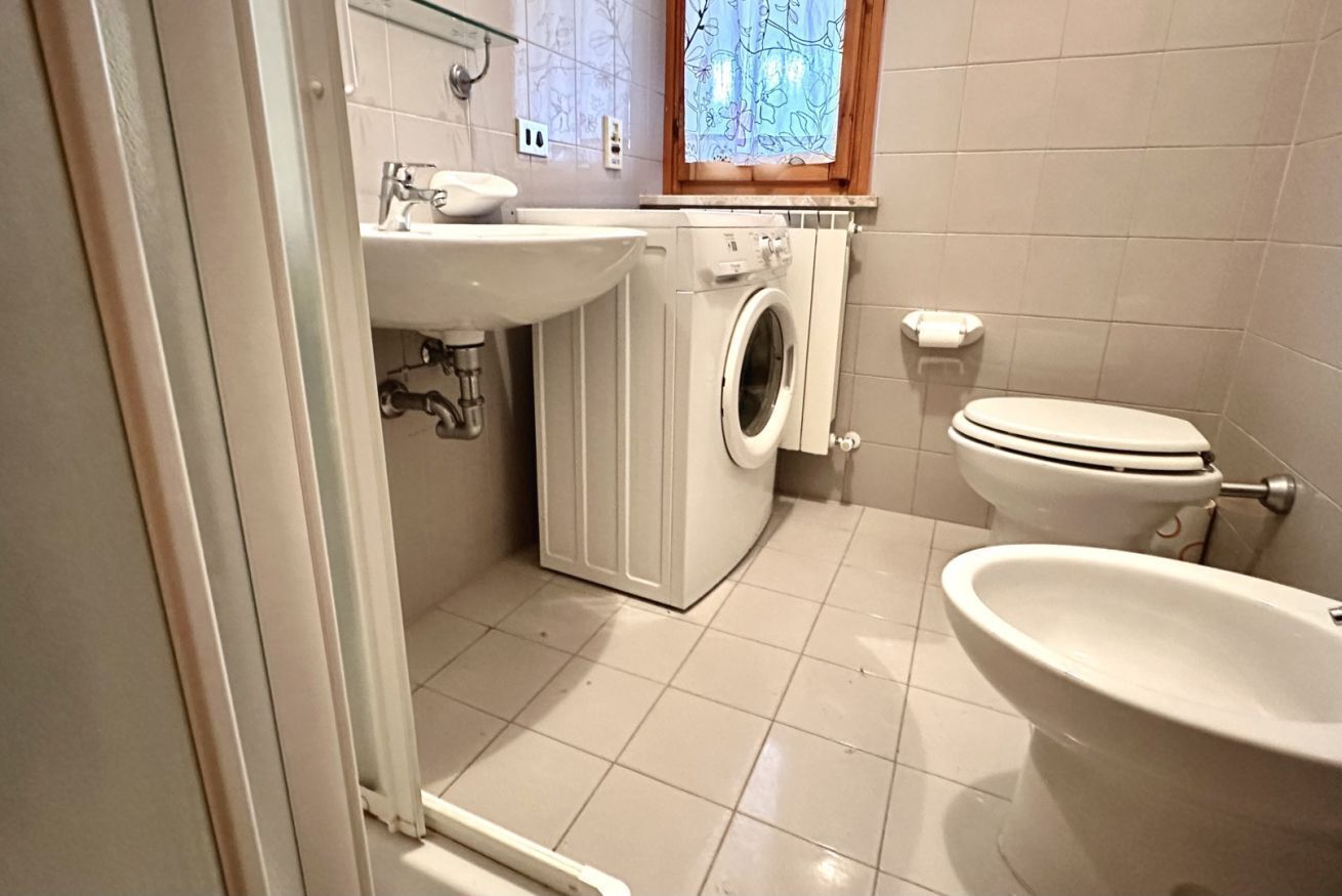 A compact bathroom with a washing machine, toilet, and sink.