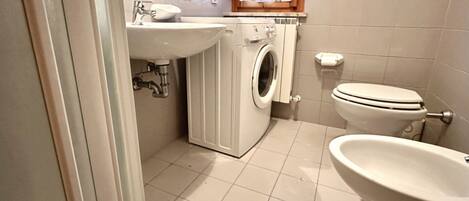 A compact bathroom with a washing machine, toilet, and sink.