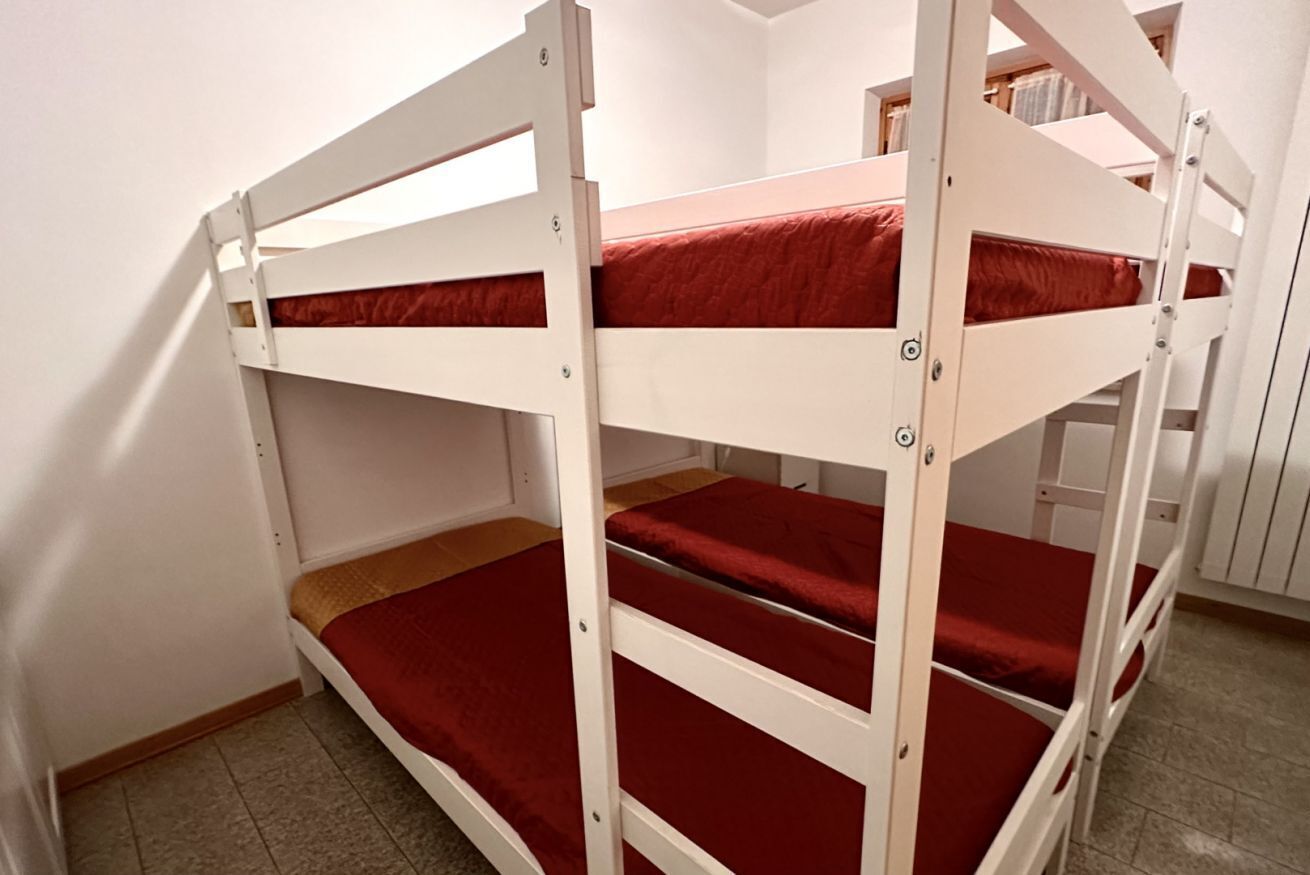 Ein Stockbett mit roter Bettwäsche in einem Zimmer mit weißen Wänden und Fliesenboden.